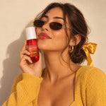 Brume parfumée corps et cheveux Vanille Caramel GUAPA tenue contre la joue par une jeune femme à lunettes et nœud satin