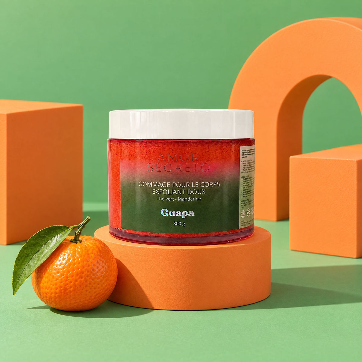 Gommage corps exfoliant doux Thé Vert Mandarine GUAPA 300 g sur blocs orange mandarine, fond vert